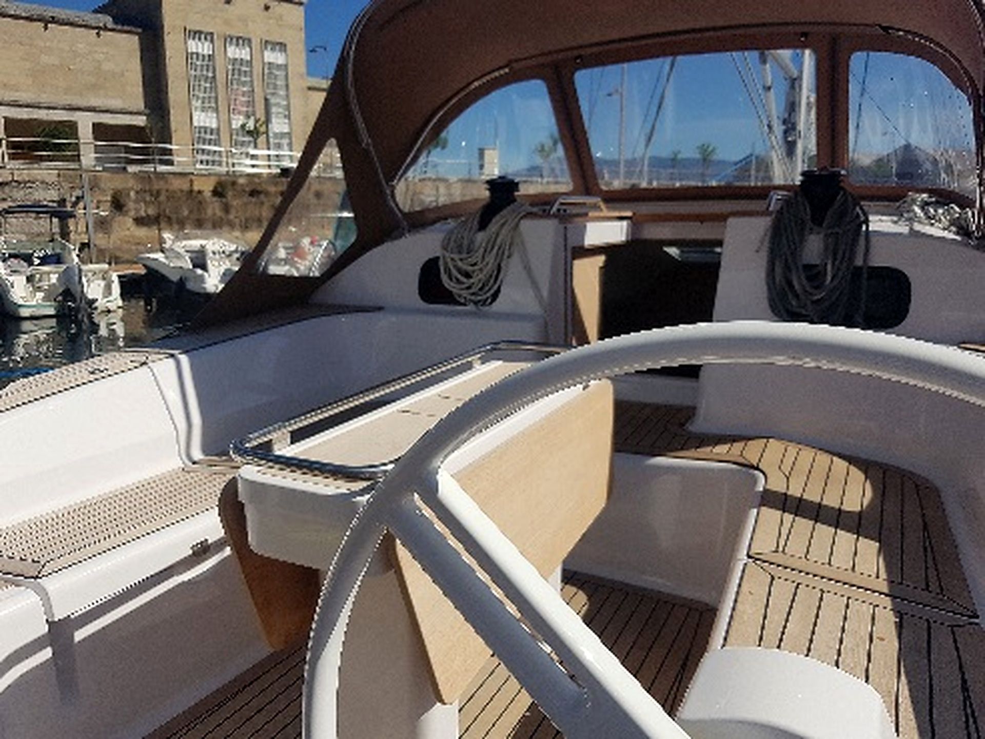 A boat's interior with a steering wheel, cushioned seating, and a view of the marina.