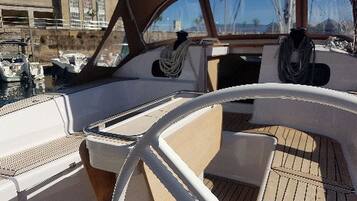 A boat's interior with a steering wheel, cushioned seating, and a view of the marina.
