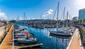 A marina with boats docked along a wooden walkway, surrounded by buildings and a clear sky.