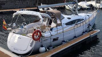 A white yacht docked at a marina with a covered deck, a steering wheel, and a lifebuoy.