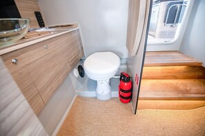 A compact bathroom with a white toilet, wooden cabinetry, a small sink, and a fire extinguisher. - Sun-Kissed Sailing Adventure in Northern Croatia (Opatija)