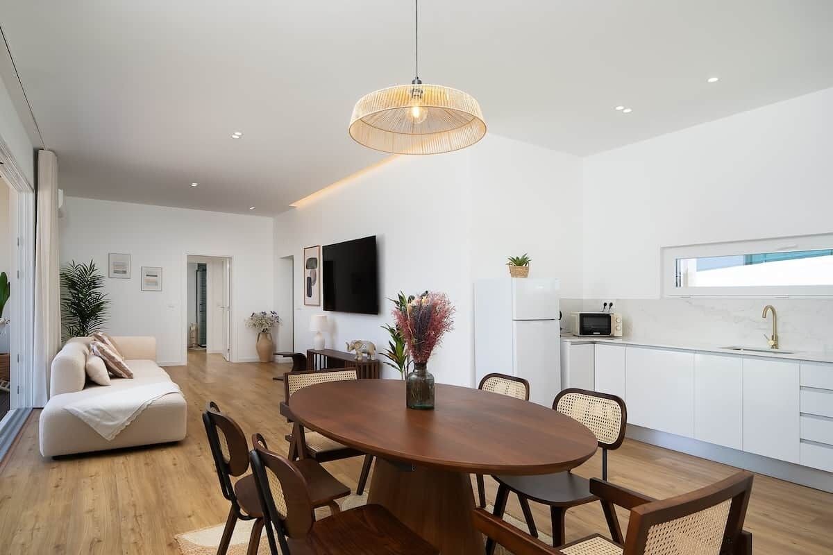 A modern living room with a dining table, chairs, a sofa, a TV, and a kitchen area.