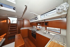 A compact kitchen with wooden cabinets, a stove, and a window overlooking the deck. - Sun-Kissed Sailing Adventure in Zadar, Croatia (Zadar)