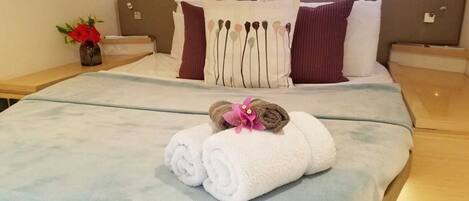 A neatly made bed with white and brown towels, a vase with flowers, and a headboard with multiple pillows.