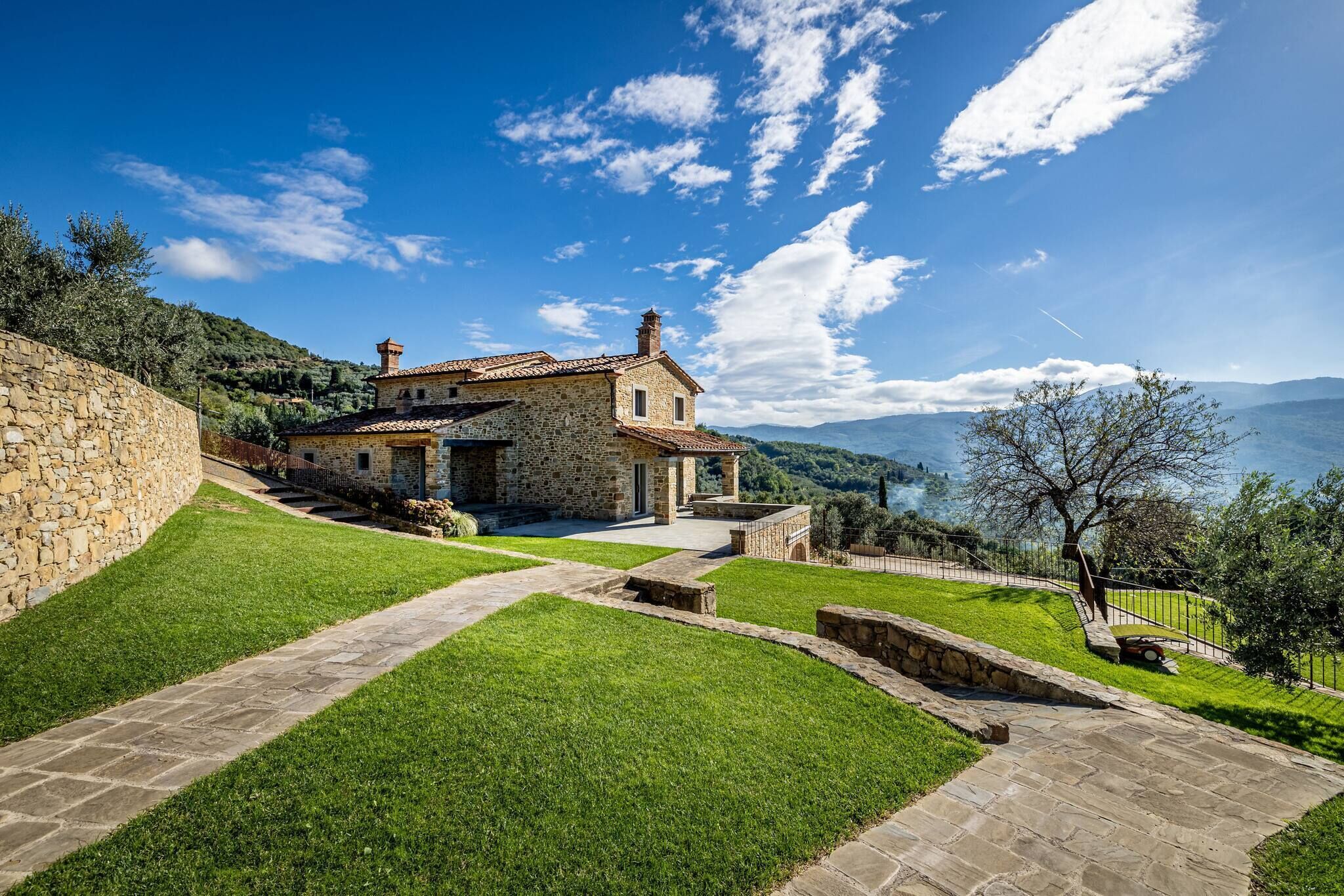 Una casa in pietra con un vialetto in pietra che conduce a una porta in legno, immersa in un prato curato e circondata da un muro di pietra.