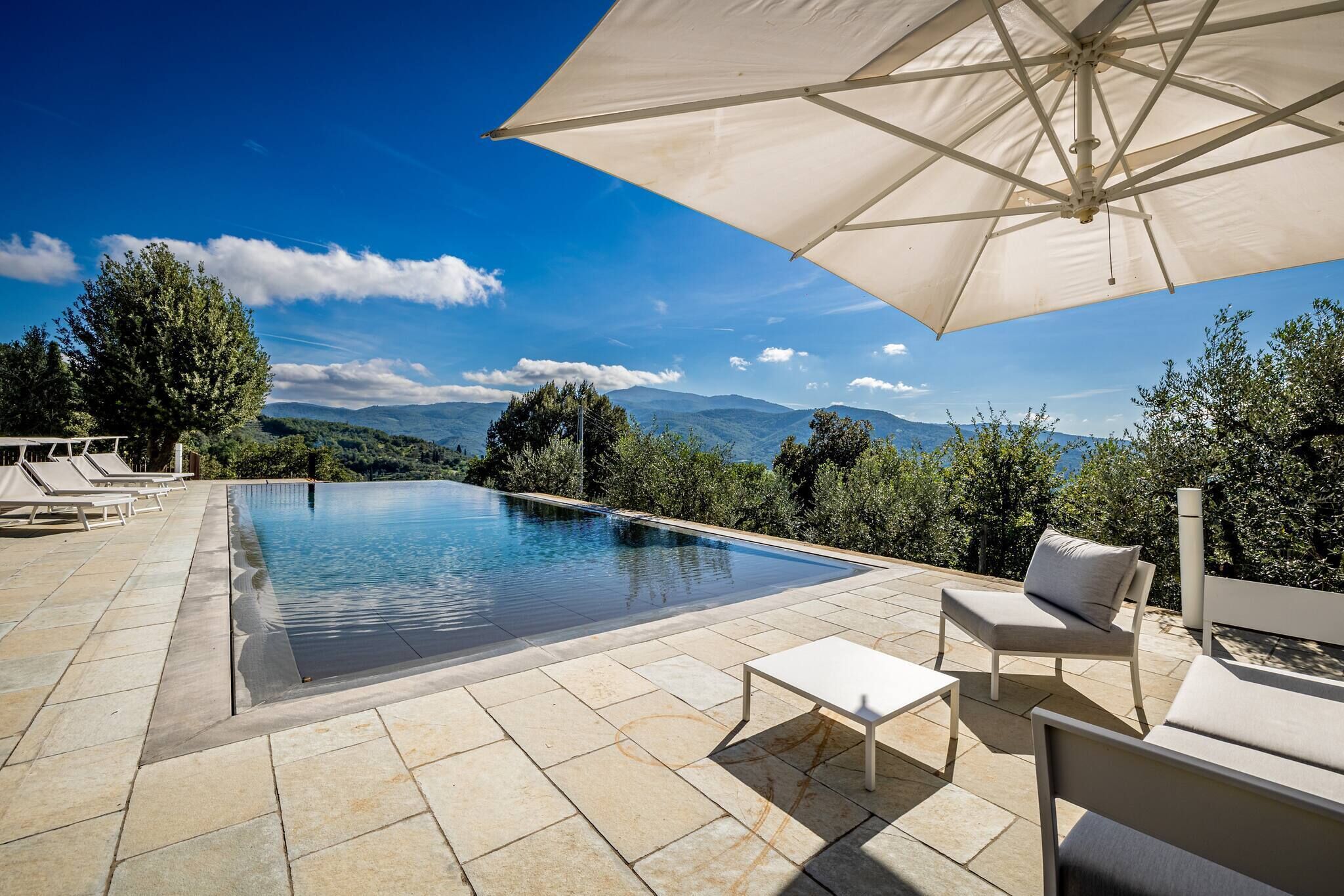 Area piscina con vista sulle montagne, un ombrellone grande e sedie a sdraio.
