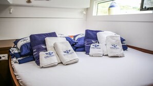 A neatly made bed with towels and pillows, a window with a view, and a small window with curtains. - Sun-Kissed Sailing Adventure in Sibenik, Croatia (Primošten)