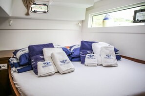 A neatly made bed with towels and pillows, a window with a view, and a small window with curtains. - Sun-Kissed Sailing Adventure in Sibenik, Croatia (Primošten)