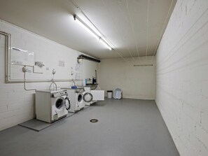 Ein Waschraum mit industriellen Waschmaschinen, einem Waschbecken und einem Mülleimer.