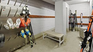 Hiihtovarastossa on telineitä, joihin on ripustettu suksia ja monot, penkki sekä seinään kiinnitetty lämmitin.