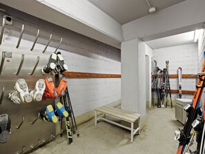 Ein Skiabstellraum mit an Regalen hängenden Skiern und Skistiefeln, einer Bank und einem Wandheizkörper.