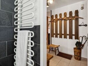 Ein Badezimmer mit weißem Handtuchhalter, einem Holzkleiderständer, einem gewebten Hocker und einer dekorativen Vase mit Pflanzen.