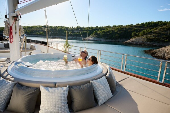 Een jacuzzi op het dek van een jacht, met uitzicht op een meer en heuvels.