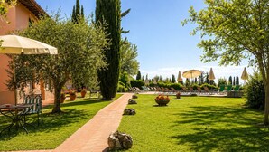 A garden with a brick pathway, outdoor seating, and lounge chairs. - Villa Vignola (Montaione)