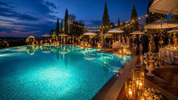 A nighttime pool area with a clear view of the pool, surrounding trees, and a distant mountain range. - Villa Vignola (Montaione)