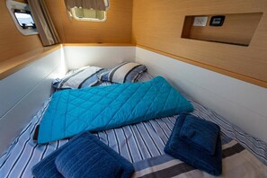 Uma cama compacta com colchão listrado, um cobertor acolchoado verde-água e duas toalhas dobradas.