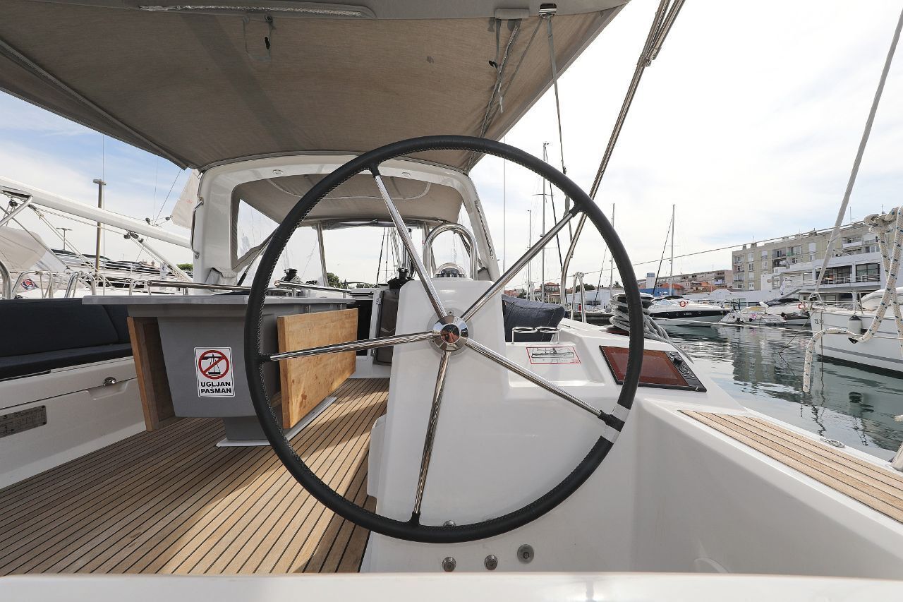 A boat's deck with a steering wheel, a wooden floor, and a sign with 'UGLIAN PASMAN' text.