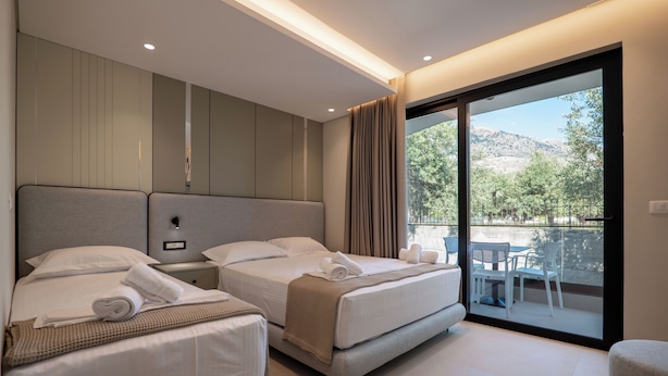 Una habitación de hotel moderna con dos camas, un balcón con mobiliario exterior y vistas al exterior.