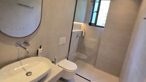 Un baño moderno con un lavamanos ovalado grande, un inodoro y una ducha con cerramiento de vidrio.
