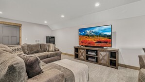 Sala de estar com sofá seccional, TV de tela plana e painel de entretenimento de madeira.