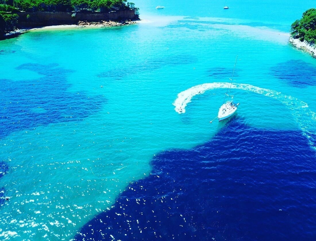 Ein Boot hinterlässt eine Bugwelle in türkisblauem Wasser, umgeben von einer Küstenlinie mit üppiger Vegetation.