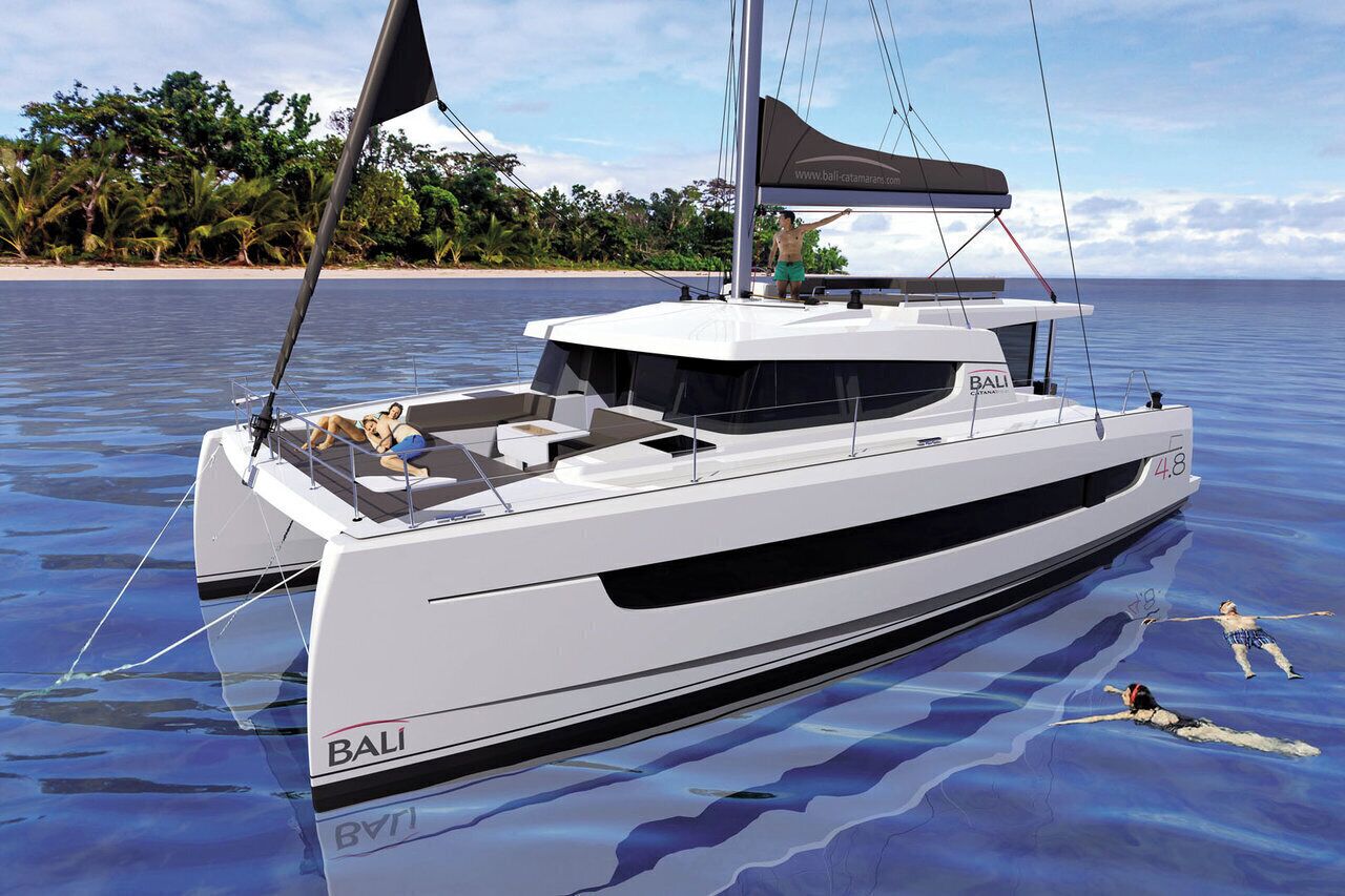 Un grand yacht portant le nom « BALI » sur sa coque, une personne debout sur le pont et une autre nageant dans l’eau.