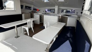 A boat interior with a dining area, white tables, and a central kitchen area. - Sun-Kissed Sailing Adventure in Phuket (Mai Khao)