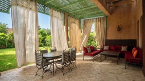 Une terrasse extérieure avec une table et des chaises en métal, un canapé rouge et une pergola agrémentée de rideaux.