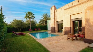 Un espace aménagé au bord de la piscine, comprenant une piscine, des chaises longues et un bâtiment doté de grandes fenêtres.