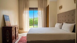 Une chambre avec un grand lit, une commode en bois et une vue sur la verdure, visible à travers une porte vitrée.