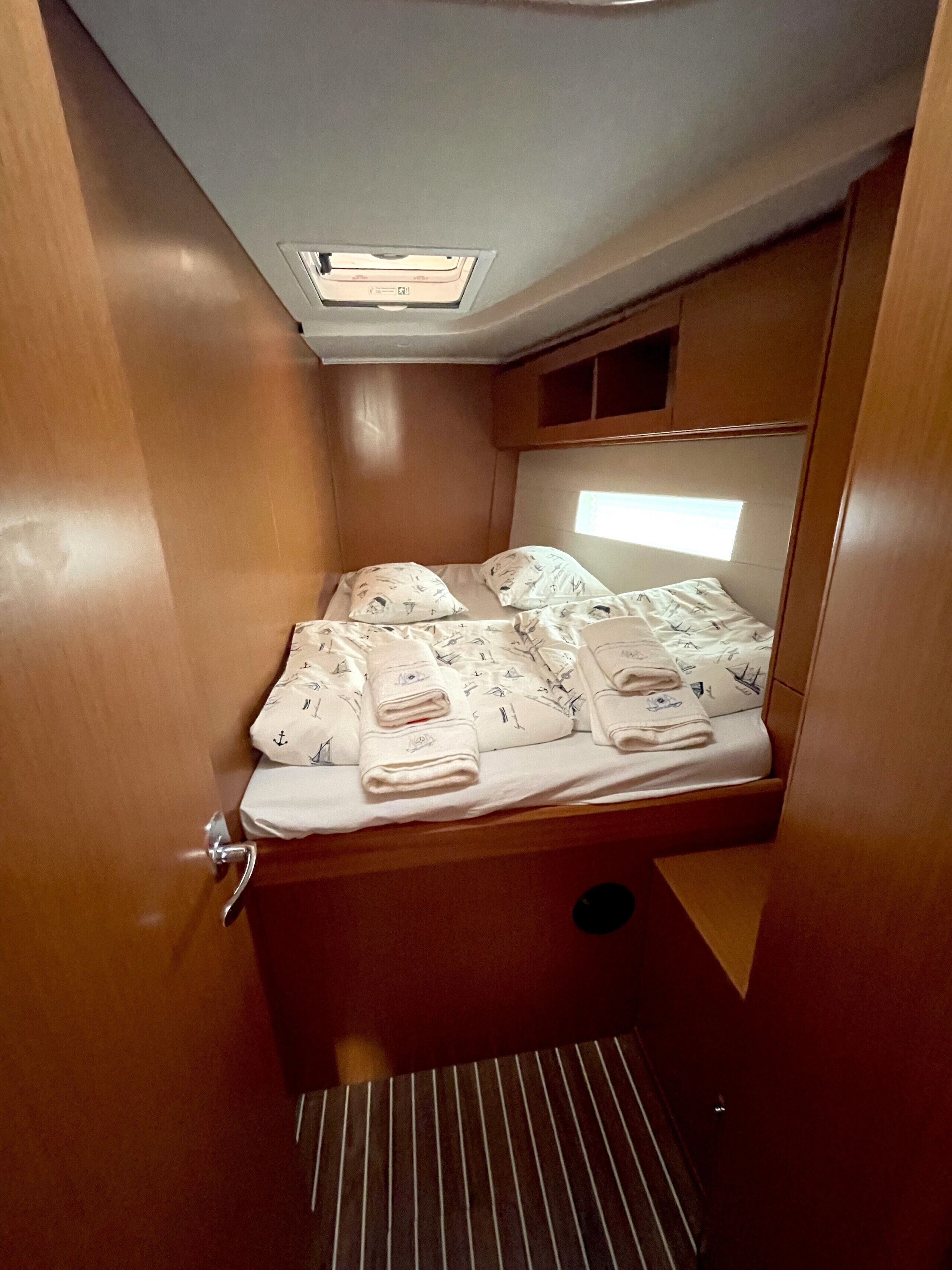 A compact, well-lit cabin with a single bed, a small window, and a ceiling light.