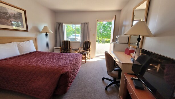 Habitación de hotel con una cama grande, un escritorio con computadora, una silla, televisor y ventana con cortinas.