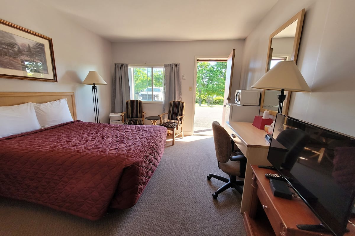 Quarto de hotel com uma cama grande, uma mesa com computador, uma cadeira, uma televisão e uma janela com cortinas.