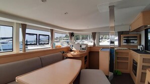 Schiffsinnenraum mit Essbereich, Küche und Fenstern mit Blick auf Boote.