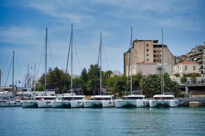 A marina with several boats docked, a building with a red roof, and a person walking on the dock. - Sun-Kissed Sailing Adventure in Islas Sarónicas (Piraeus)