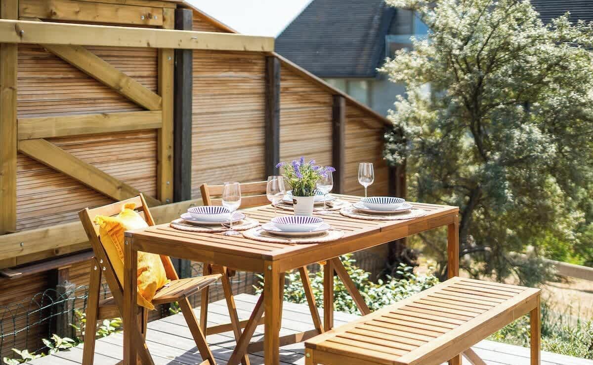 Eine Holzterrasse mit einem Tisch für vier Personen, umgeben von Holzstühlen und einer Bank.