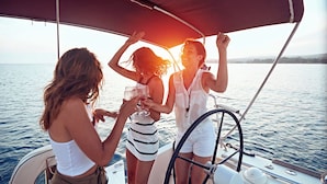 Eine Segelyacht mit Sonnensegel, Personen mit Getränken und ruhiges Meer.