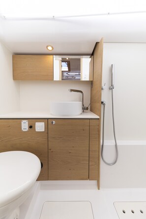 Een moderne badkamer met een houten wastafelmeubel, een witte wastafel, een toilet en een douche.