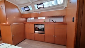 A compact galley with a stove, two overhead monitors, and wooden cabinetry. - Sun-kissed Sailing Adventure in Split-Dalmatia, Croatia (Trogir)