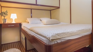 A neatly made bed with a pillow, a bedside lamp, and a small potted plant on a wooden nightstand. - Sun-Kissed Sailing Adventure in Split, Croatia (Split)