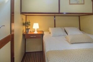 Ein Hotelzimmer mit Bett, Nachttisch mit Lampe, Topfpflanze und kleiner Schublade.
