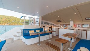 L’intérieur d’un yacht comprenant un coin salon, une petite cuisine et une vue sur la mer.