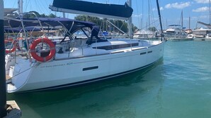 Eine weiße Segelyacht namens 'SUN ODYSSEY 409' liegt in einer Marina, im Hintergrund sind weitere Boote zu sehen.