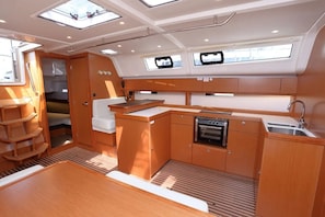 A compact galley with a stove, sink, and seating area, featuring a skylight and wooden cabinetry.