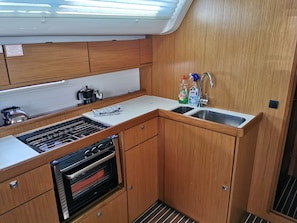 Una cocina compacta con armarios de madera, horno empotrado, lavamanos y una ventana sobre la encimera.