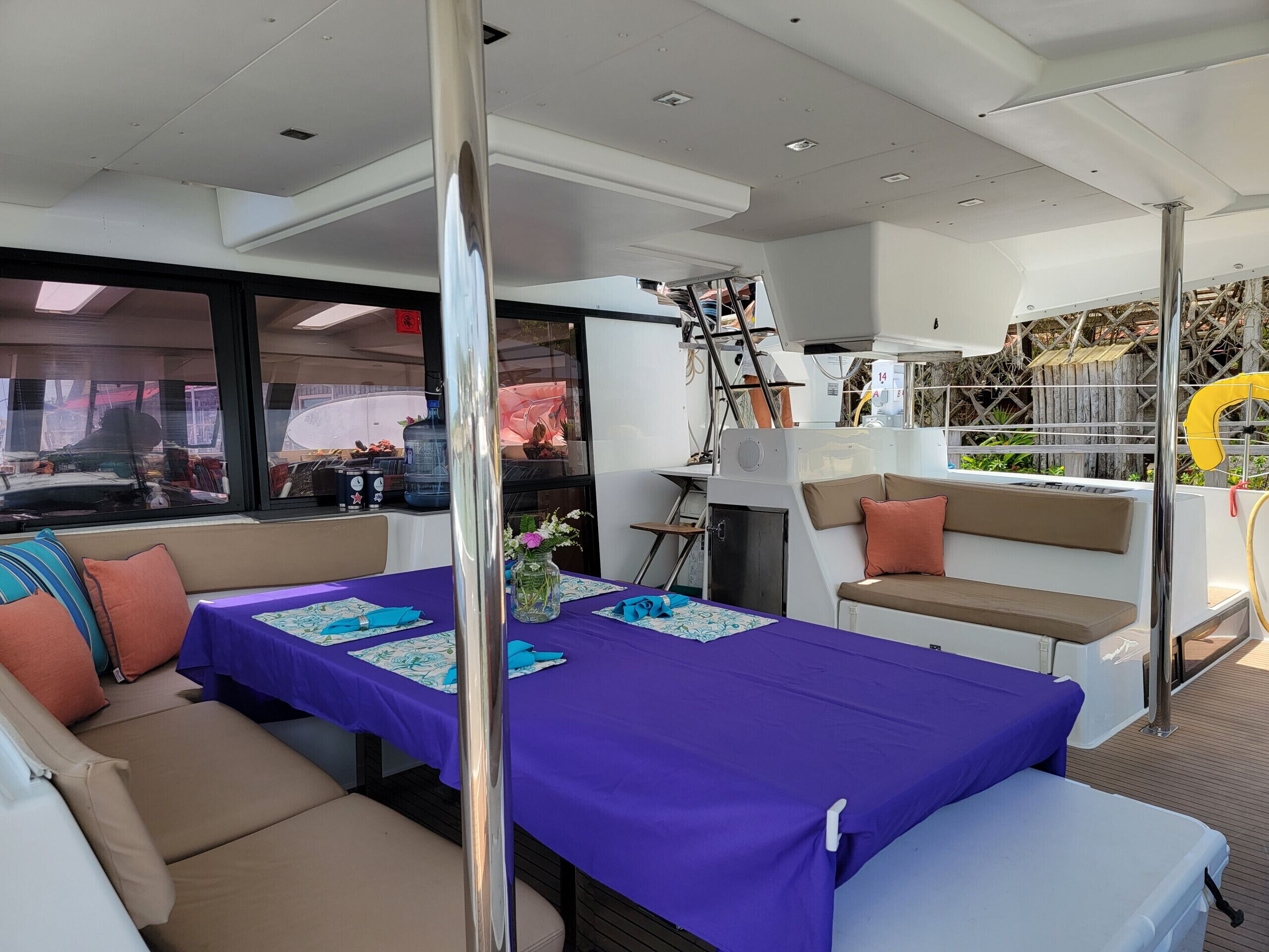 Interior de barco com mesa posta para refeição, assentos acolchoados e vista através de grandes janelas.