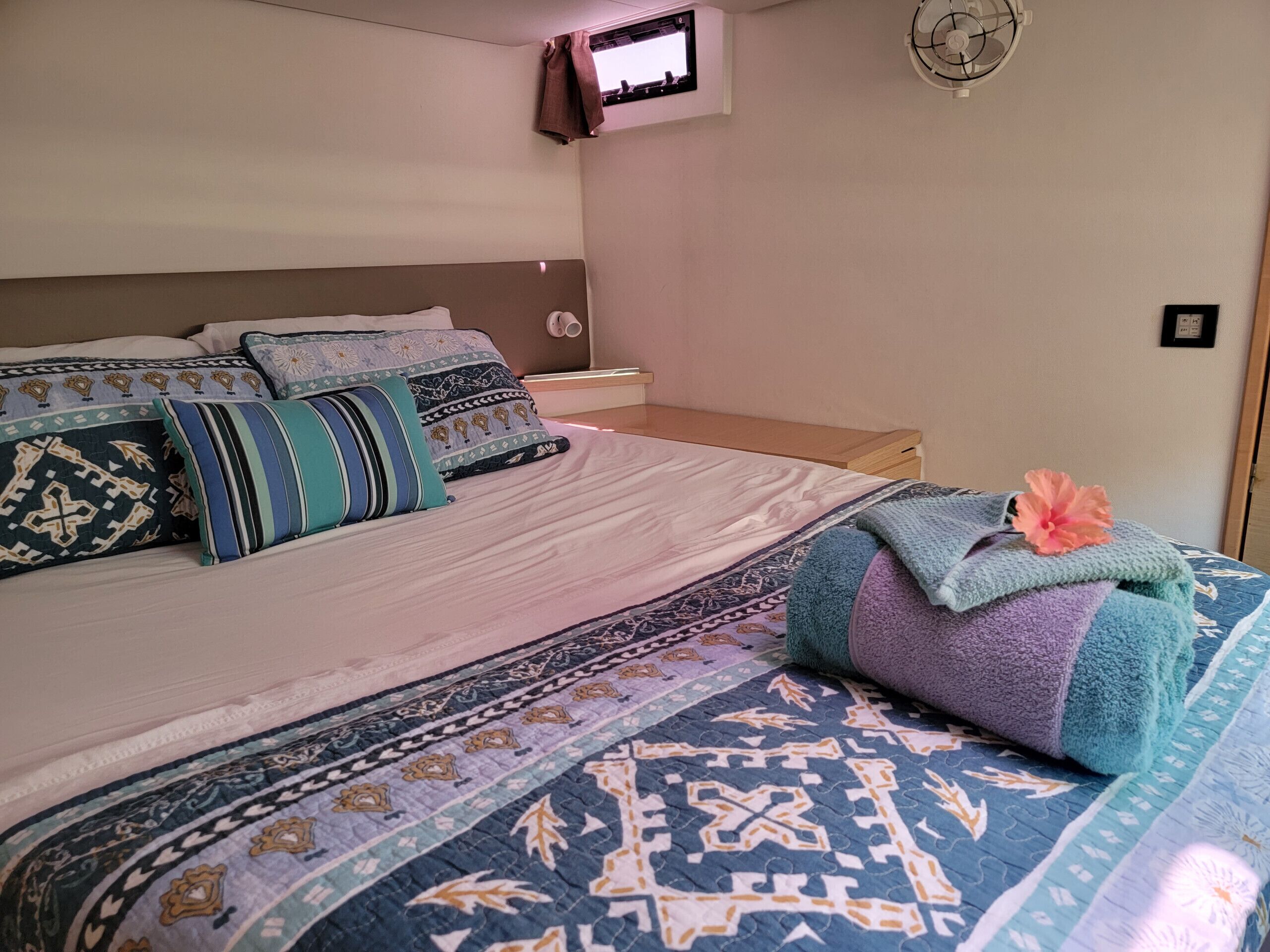 A bed with patterned bedding, a nightstand, a wall-mounted TV, and a ceiling fan.