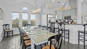 A spacious dining area with a glass table, black chairs, and a modern chandelier.