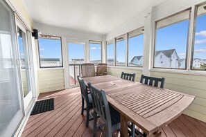 A covered outdoor dining area with a wooden table and chairs, large windows, and a view of houses. - Good Latitude (Avon)
