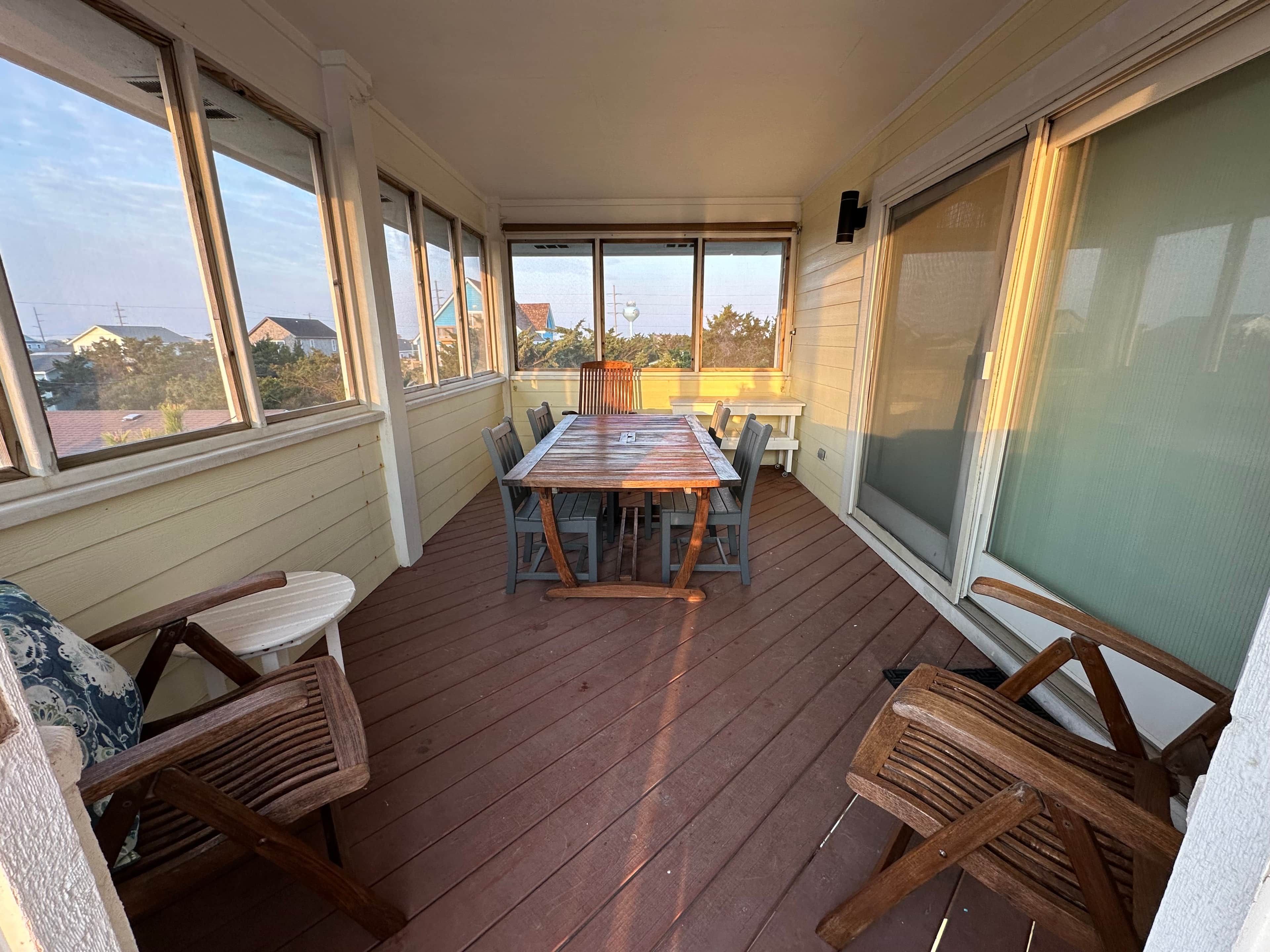 A covered patio with a wooden table and chairs, large windows, and a view of the neighborhood.